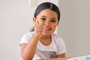 Young girl smiling with thumbs up while fingerpainting