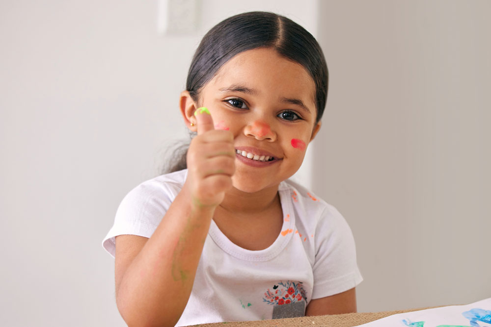 Young girl smiling with thumbs up while fingerpainting