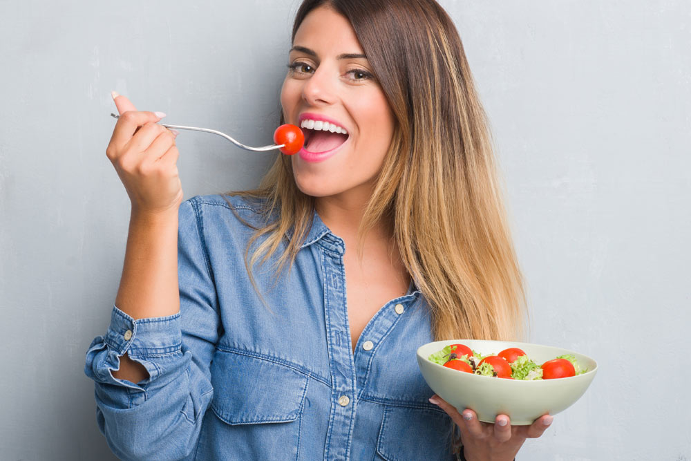 Smiling young woman eating healthy salad